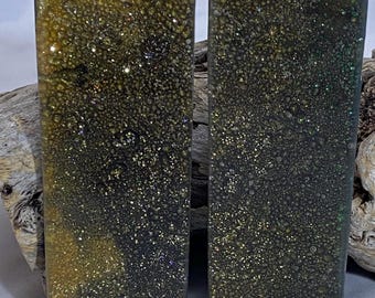 Op de afbeelding: Twee rechthoekige harsstukken met een gespikkelde, glinsterende uitstraling. De hars is voornamelijk donkergroen en goudkleurig, met een textuur. De stukken worden getoond tegen een natuurlijke houten achtergrond.