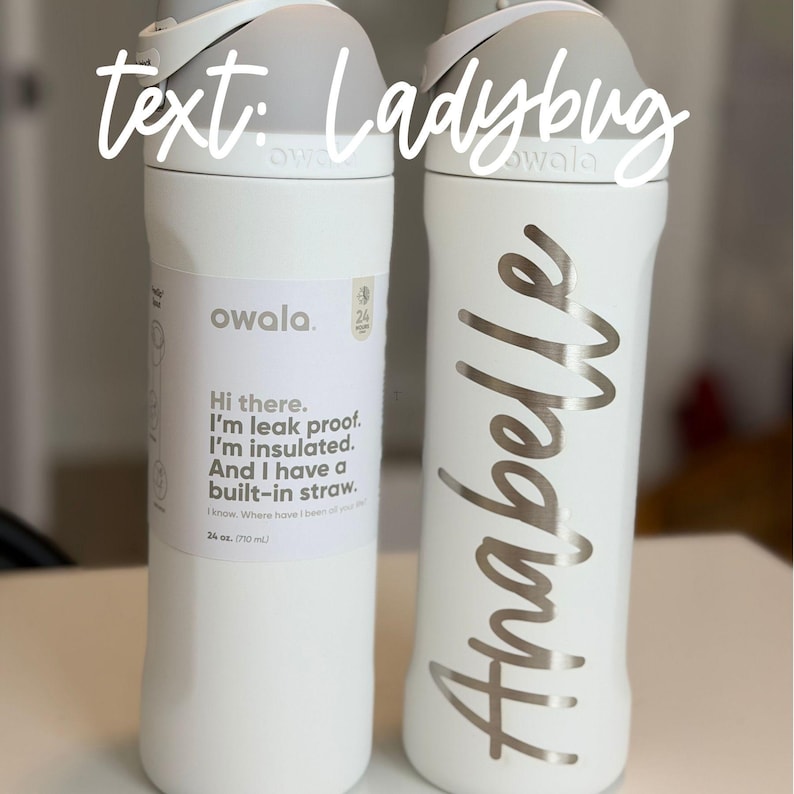 May include: Two white Owala insulated water bottles. One bottle has the name "Anabelle" in silver script. The other bottle has text that reads "Hi there. I'm leak proof. I'm insulated. And I have a built-in straw." The bottles are 24 oz (710 mL).