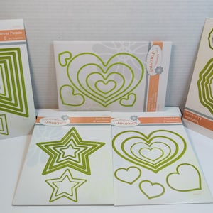 May include: Five different die-cut metal stencils for crafting. The stencils are on white cardstock with green outlines of hearts, stars, banners, and circles. The cardstock has the text "Fun Stampers Journey" printed on it.