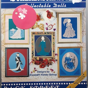 May include: A collection of framed paper cutouts of women in period clothing, with a pink circular tag with flower cutouts. The title "SCHERENSCHNITTE Collectable Dolls" is displayed above the images. The words "BACK STREET DESIGNS" are at the bottom.