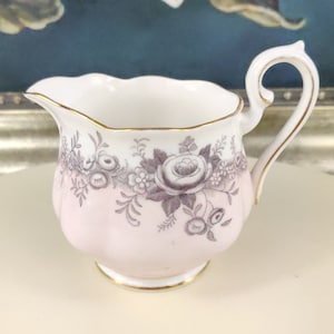 Peut inclure: Un petit pot à crème blanc avec un motif floral rose et gris. Le pot à crème a un bord festonné et une bordure dorée.
