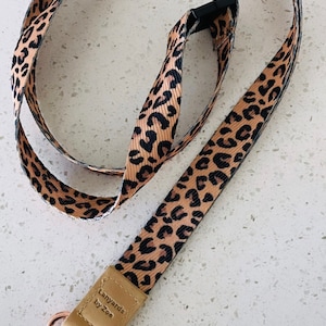 May include: A brown and black leopard print lanyard with a gold-coloured clasp and a brown leather tag that says "Lanyards by Zoe".