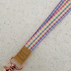 May include: A colourful striped lanyard with a brown leather tag that says "Lanyards by Zoe" and a rose gold metal clip.