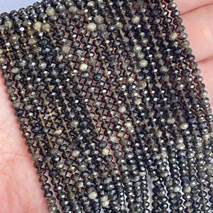 May include: A strand of black and gold gemstone beads. The beads are faceted and have a shiny finish. The beads are strung on a thin wire.