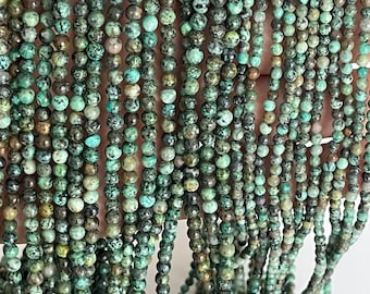 May include: A strand of turquoise beads, each bead is a mottled green and brown color. The beads are round and have a smooth, polished finish.