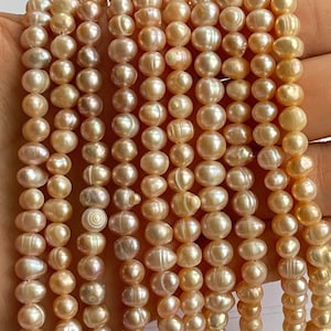 Könnte beinhalten: Eine Strähne aus hellrosa Süßwasserperlen, jede Perle ist rund und glatt mit einem leichten irisierenden Schimmer. Die Perlen sind auf einem durchsichtigen Faden aufgefädelt und bereit für die Schmuckherstellung.