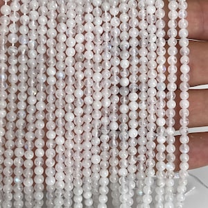 May include: Strands of small, round, white beads with a subtle iridescent sheen. The beads are strung together, creating a delicate and elegant appearance. The beads are likely used for jewelry making or crafting.