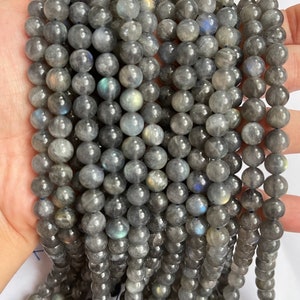 May include: A strand of grey labradorite gemstone beads. The beads are round and have a smooth, polished finish. The labradorite has an iridescent sheen, with flashes of blue, green, and gold.