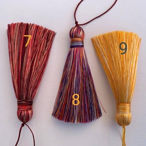 May include: Three colourful tassel ornaments with a striped design. The tassels are numbered 7, 8, and 9.