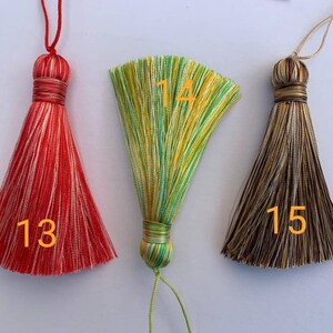 May include: Three tassel ornaments with different colour combinations. The first tassel is red and white, the second is green and yellow, and the third is brown and white. The tassels are numbered 13, 14, and 15.