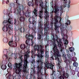 May include: A strand of purple, pink and green fluorite beads. The beads are round and have a smooth, polished finish.