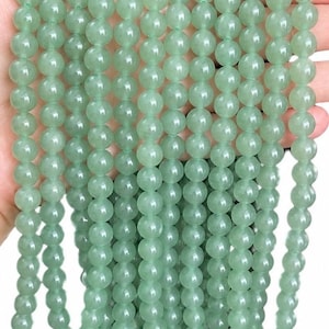 May include: A collection of multiple strands of smooth, round, light green aventurine beads. Each bead features a polished, semi-translucent finish with subtle natural variations in colour, arranged in vertical rows to showcase the uniform shape.