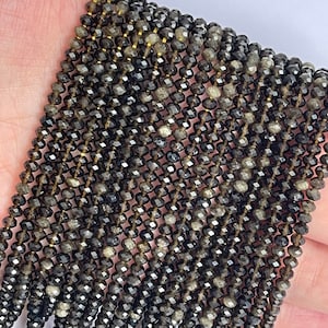 May include: A strand of black faceted gemstone beads. The beads are small and have a slightly iridescent sheen.