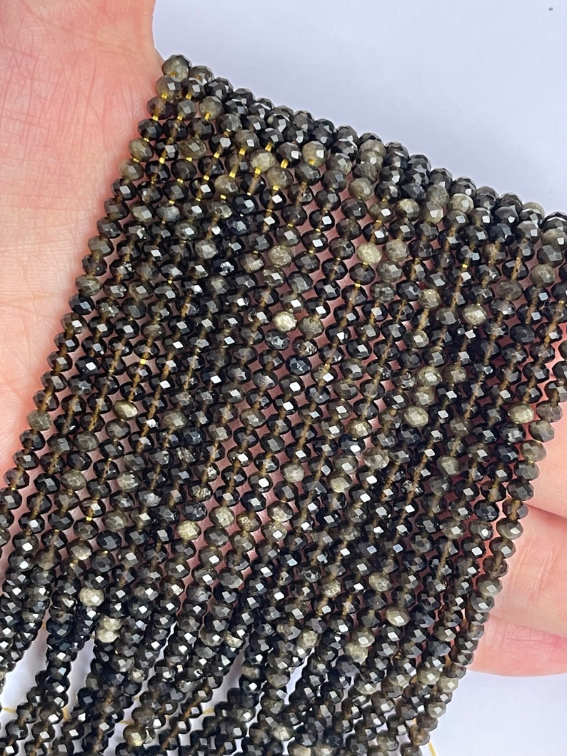 May include: A strand of black faceted gemstone beads. The beads are small and have a slightly iridescent sheen.