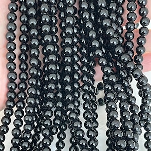May include: Multiple strands of shiny, black beads. The beads are spherical and consistent in size, threaded together to form a flowing, dark arrangement. The beads reflect light, giving them a polished look. Suitable for jewellery making.