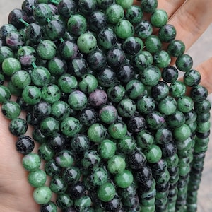 May include: A strand of green and black gemstone beads. The beads are round and have a speckled appearance.