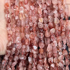 May include: A strand of translucent, reddish-brown, tumbled gemstone beads. The beads are irregularly shaped and have a natural, rough texture.