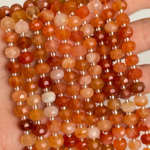Pode incluir: Um fio de contas de cornalina, com uma mistura de tons laranja e vermelho. As contas são facetadas e têm um acabamento polido.
