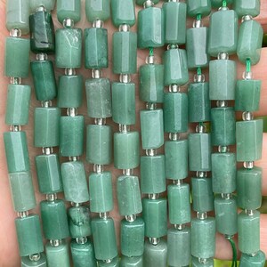 May include: A strand of green jade beads, each bead is a rectangular prism shape with slightly rounded edges. The beads are strung on a clear elastic cord.