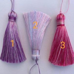 May include: Three colourful tassel ornaments with white and purple, white and pink, and white and red stripes. The tassels are numbered 1, 2, and 3.