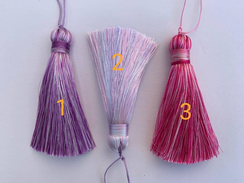 May include: Three colourful tassel ornaments with white and purple, white and pink, and white and red stripes. The tassels are numbered 1, 2, and 3.