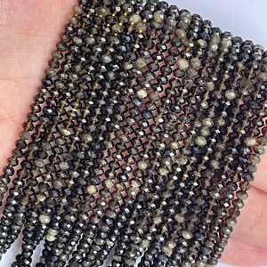 May include: A strand of black faceted gemstone beads. The beads are small and have a slightly iridescent sheen.