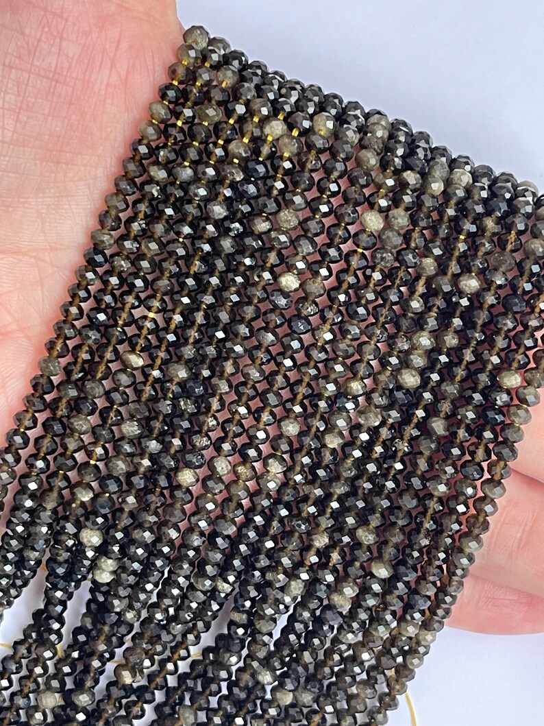 May include: A strand of black faceted gemstone beads. The beads are small and have a slightly iridescent sheen.