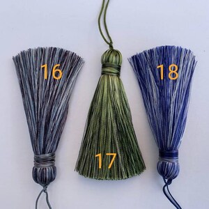 May include: Three tassel ornaments with different colour combinations. The tassel on the left is blue and white, the middle tassel is green and black, and the tassel on the right is blue and white. The tassels are numbered 16, 17, and 18.