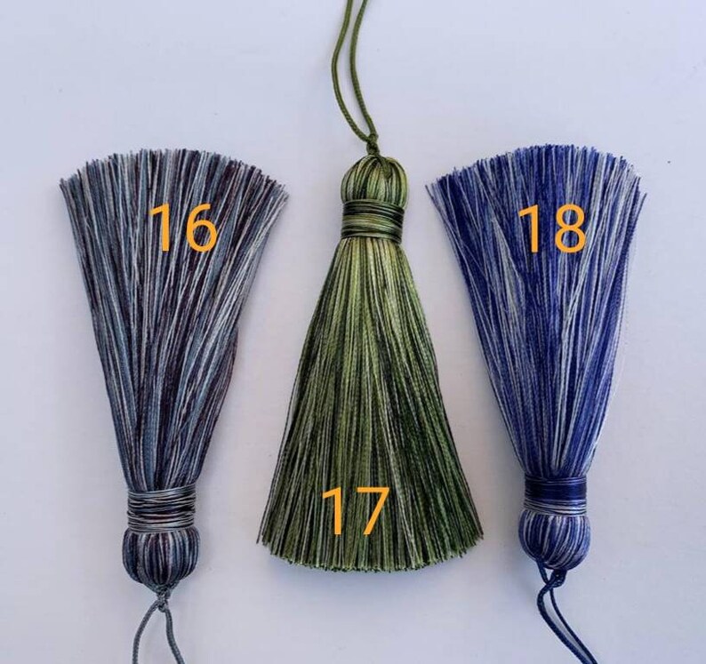 May include: Three tassel ornaments with different colour combinations. The tassel on the left is blue and white, the middle tassel is green and black, and the tassel on the right is blue and white. The tassels are numbered 16, 17, and 18.