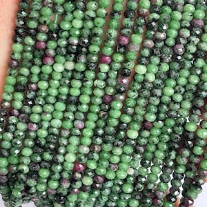 Op de afbeelding: Een streng groene, zwarte en roze facetgeslepen edelsteen kralen. De kralen zijn rond en hebben een gladde, gepolijste afwerking.