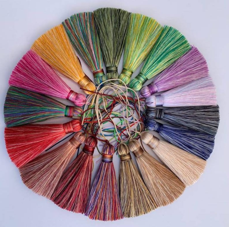 May include: A collection of 15 colourful tassel trims in various shades of green, blue, red, pink, yellow, and brown. The tassels are arranged in a circle, with the tips of the tassels pointing outwards.