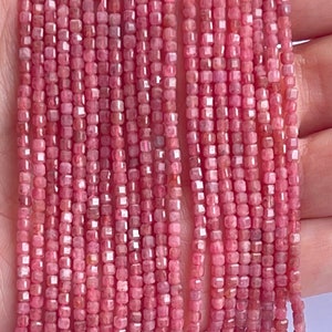 May include: A strand of pink rhodochrosite gemstone beads, each bead is faceted and square shaped. The beads are strung on a clear thread.