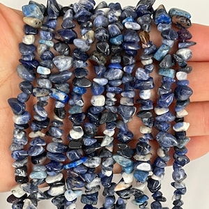 May include: A strand of blue, white and black gemstone chips. The chips are irregularly shaped and have a natural, rough texture.