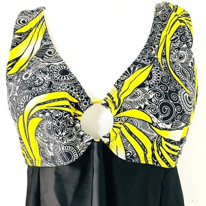 Puede incluir: Un ba&ntilde;ador de una pieza con falda negra y top con dise&ntilde;o estampado en amarillo, negro y blanco. El top tiene un escote pronunciado con un detalle de anillo dorado. El ba&ntilde;ador se exhibe en un maniqu&iacute; blanco.