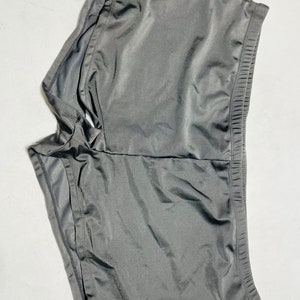 Puede incluir: Un par de pantalones cortos deportivos de color gris oscuro. Los pantalones cortos est&aacute;n hechos de una tela suave y brillante y tienen una cintura el&aacute;stica. Los pantalones cortos est&aacute;n dise&ntilde;ados para la comodidad y el movimiento.