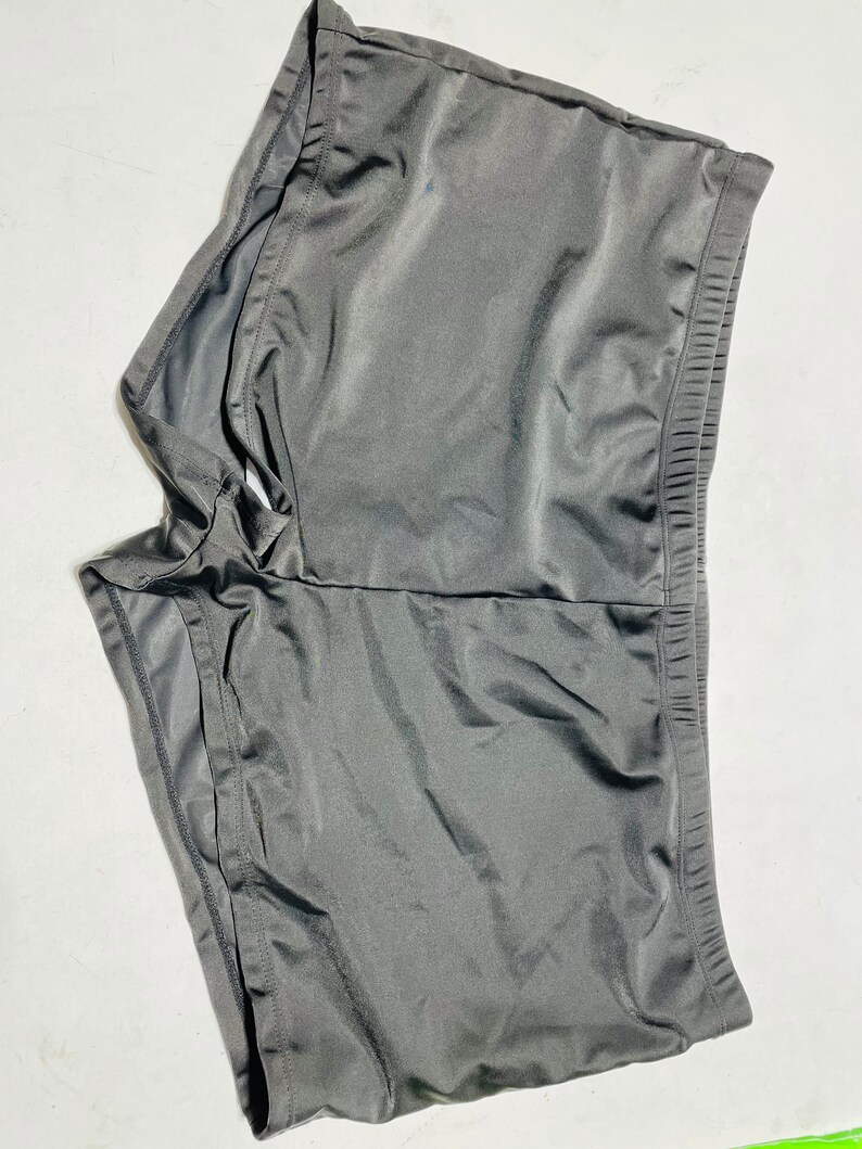 Puede incluir: Un par de pantalones cortos deportivos de color gris oscuro. Los pantalones cortos est&aacute;n hechos de una tela suave y brillante y tienen una cintura el&aacute;stica. Los pantalones cortos est&aacute;n dise&ntilde;ados para la comodidad y el movimiento.