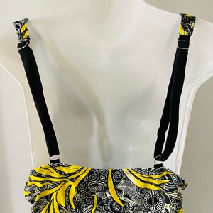 Puede incluir: Top de traje de ba&ntilde;o negro con un dise&ntilde;o estampado en amarillo y negro. El top tiene tirantes negros ajustables y una secci&oacute;n inferior negra lisa. Las correas est&aacute;n unidas con anillos de metal plateado. El patr&oacute;n incluye dise&ntilde;os en espiral.