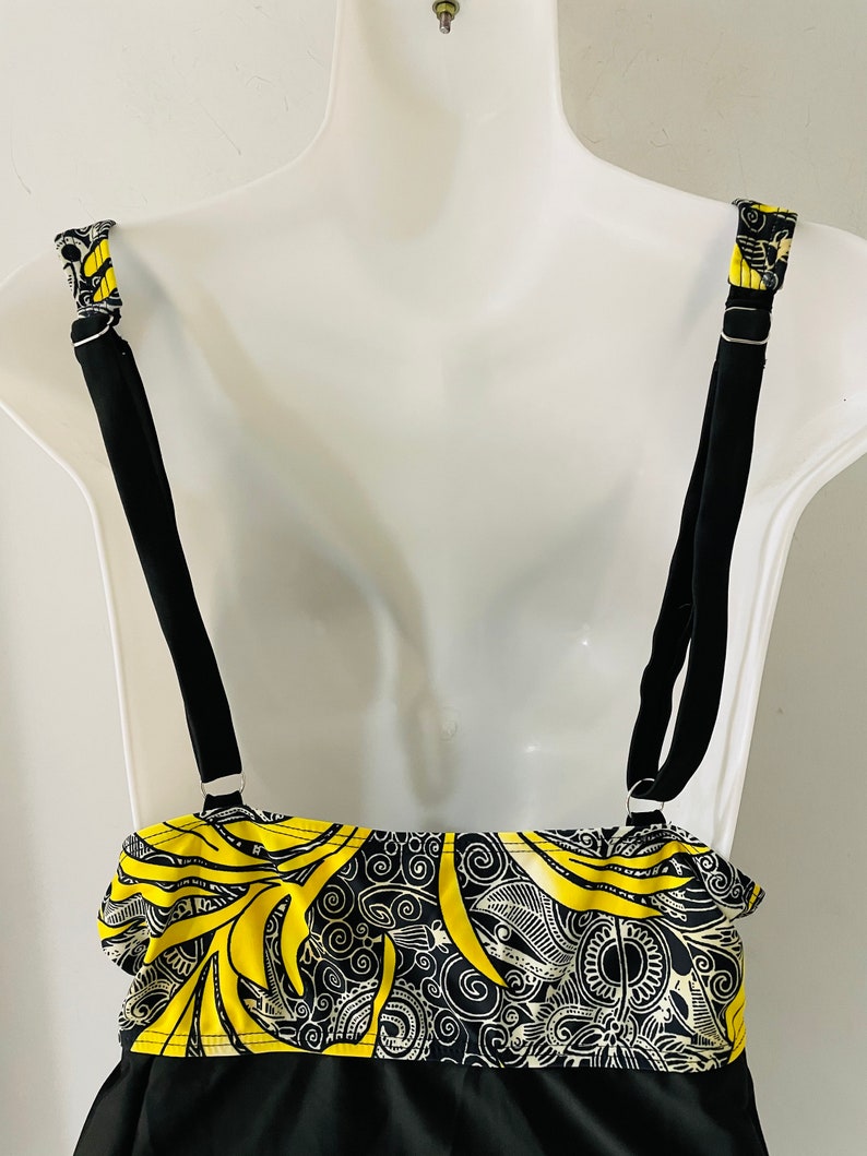Puede incluir: Top de traje de ba&ntilde;o negro con un dise&ntilde;o estampado en amarillo y negro. El top tiene tirantes negros ajustables y una secci&oacute;n inferior negra lisa. Las correas est&aacute;n unidas con anillos de metal plateado. El patr&oacute;n incluye dise&ntilde;os en espiral.