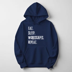 May include: A navy blue hoodie with a front pocket and a drawstring. The white text on the front reads: EAT. SLEEP. WORDSCAPES. REPEAT. A casual, comfortable garment for everyday wear.
