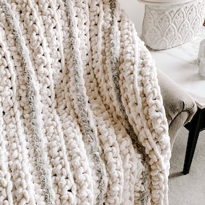 Puede incluir: Una manta de punto de crochet a rayas blancas y grises con una textura esponjosa.