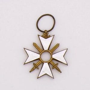 May include: A gold-toned pendant in the shape of a cross with white enamel sections and two swords. The pendant has a circular loop at the top for hanging. The cross design is centered with a circular element.