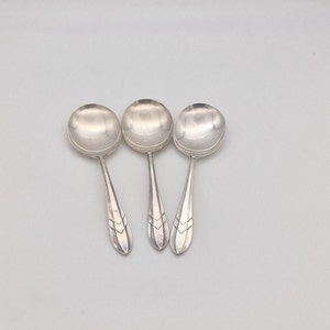 Puede incluir: Tres cucharas de plata con mangos adornados. Las cucharas tienen una forma de cuenco redondeada y un mango ligeramente curvado.