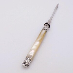 May include: A vintage letter opener with a mother-of-pearl handle and silver-coloured metal detailing. The blade is slender and pointed. The handle is cylindrical with decorative bands at each end.