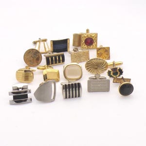 May include: A collection of vintage cufflinks in various shapes and designs. The cufflinks are gold, silver, black, and red. Some feature geometric patterns, while others have textured surfaces or gemstone accents. A few have a coin design.
