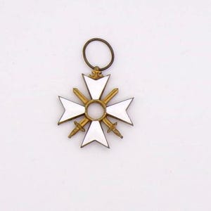May include: A white and gold cross-shaped pendant with a circular loop at the top. The pendant features a white enamel cross design with gold swords and a central gold ring. The overall design is symmetrical and detailed.