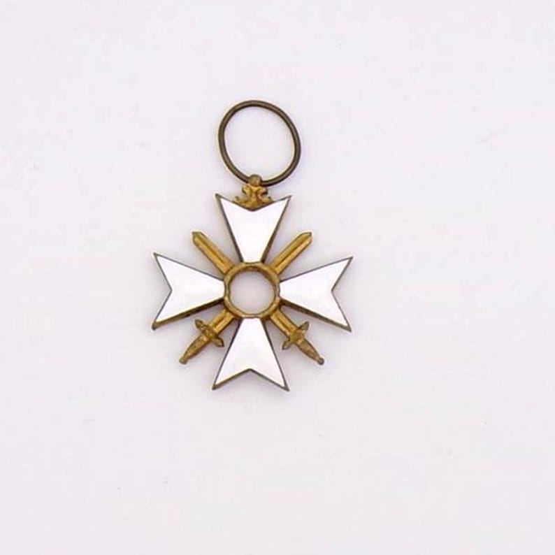 May include: A white and gold cross-shaped pendant with a circular loop at the top. The pendant features a white enamel cross design with gold swords and a central gold ring. The overall design is symmetrical and detailed.