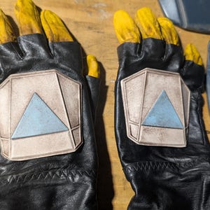 May include: A pair of black leather gloves with yellow accents and a gray triangle design on the back of each hand.