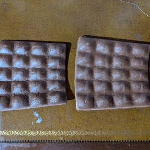 May include: Two brown, rectangular, textured, waffle-like baking sheets. The sheets are slightly curved and have a light brown color.