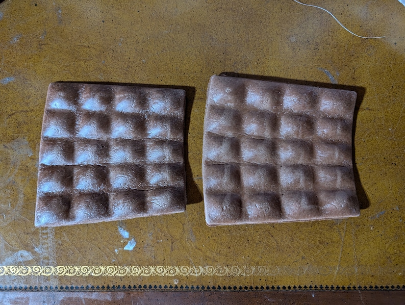May include: Two brown, rectangular, textured, waffle-like baking sheets. The sheets are slightly curved and have a light brown color.