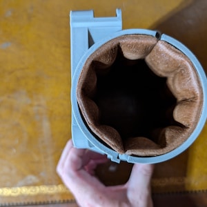 May include: A gray 3D printed cup holder with a brown leather lining.
